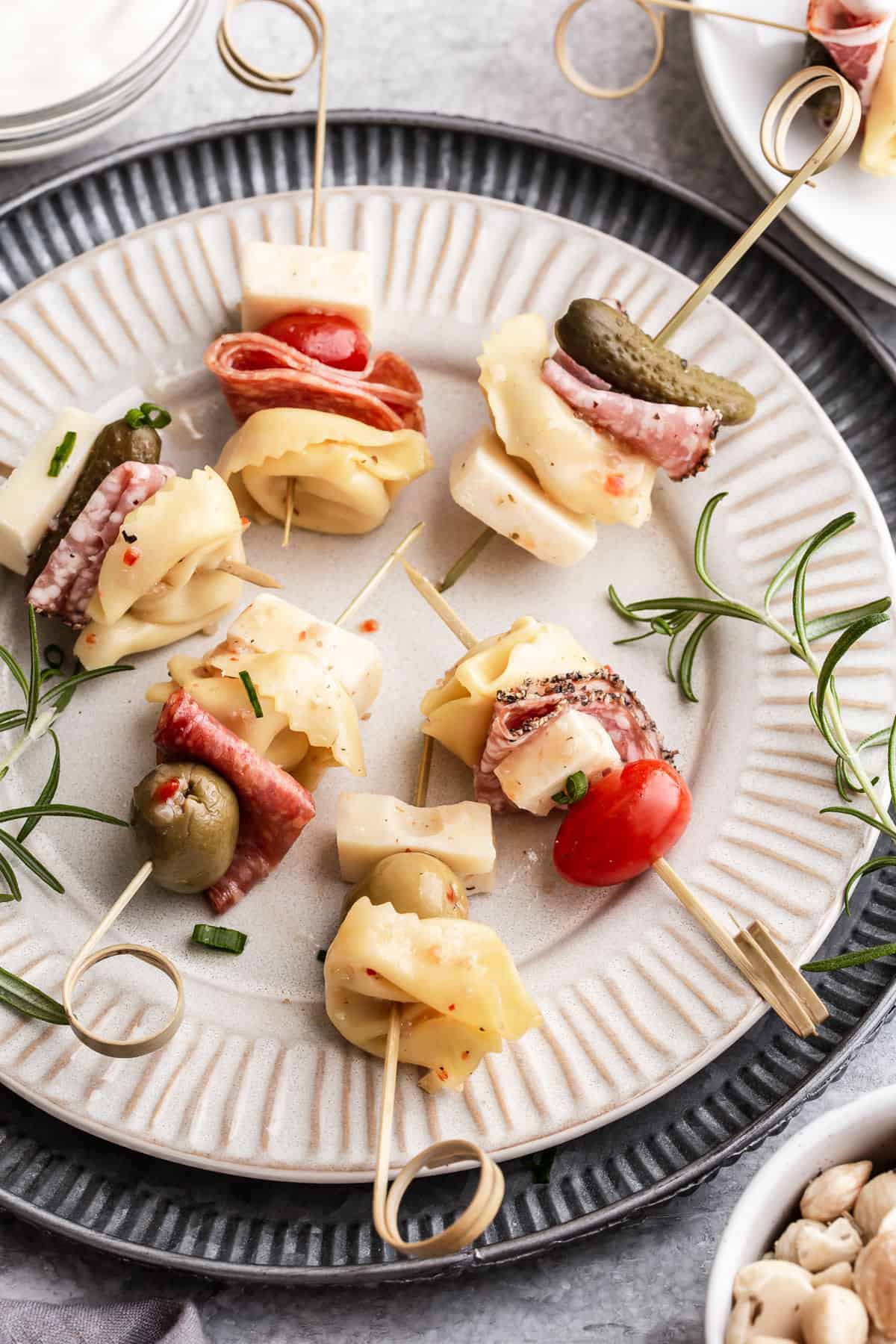 small skewers with tortellini, meats, cheese and pickled veggies, on tan plate.