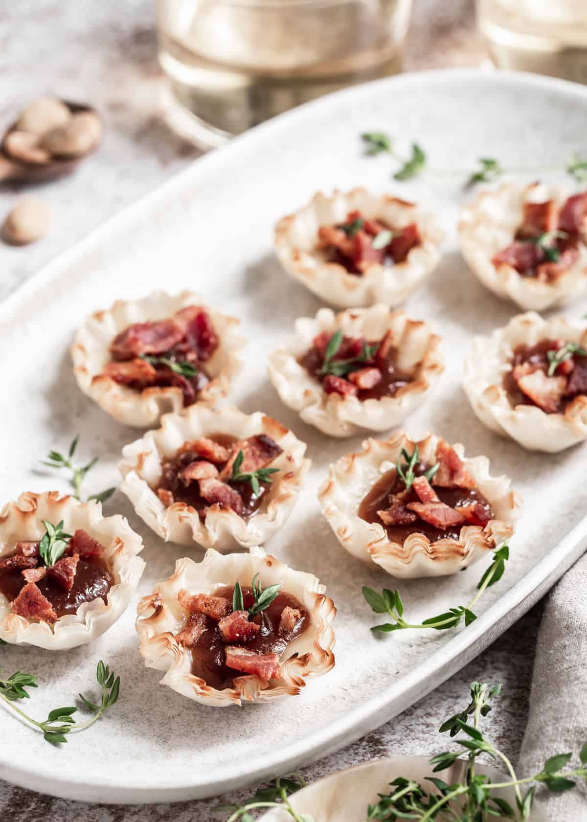 phyllo shells with brie, apple butter and crumbled bacon, on white platter.
