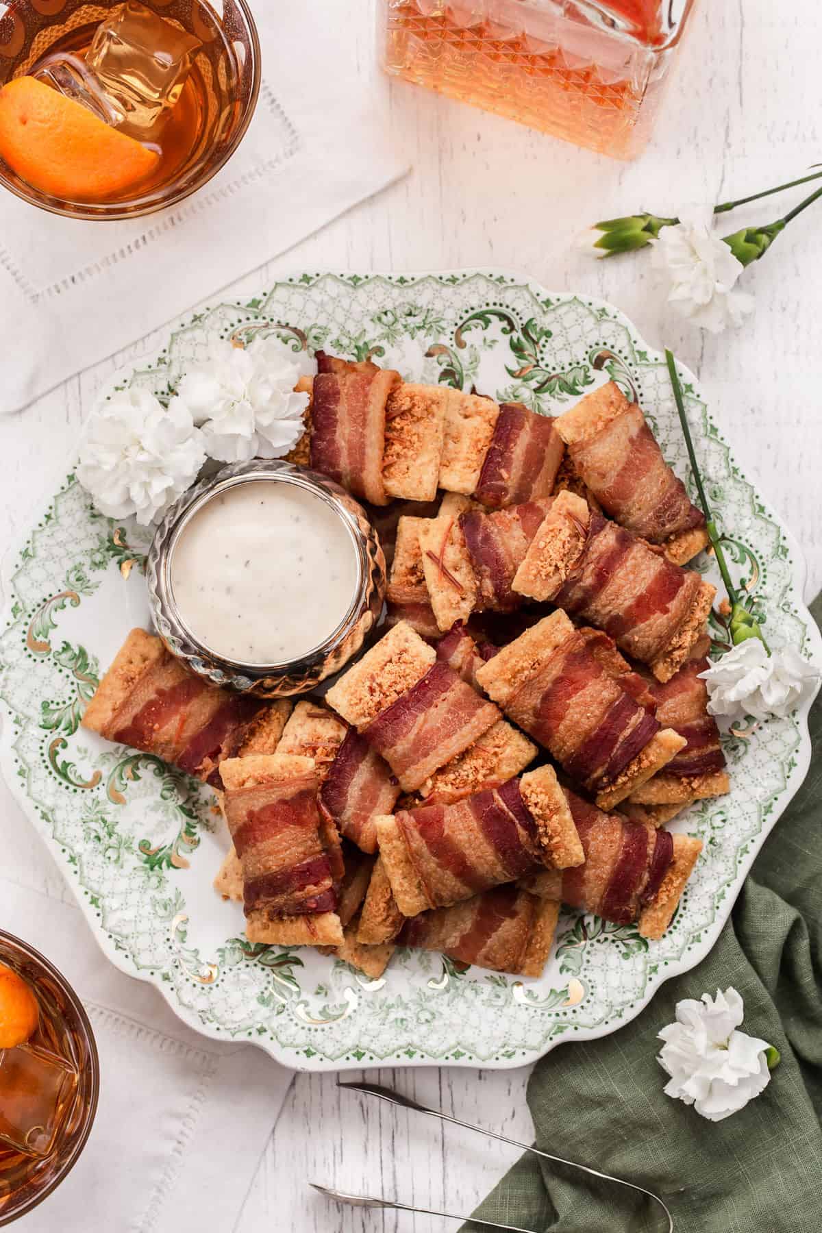 pile of bacon wrapped crackers on green and white vintage plate with small dip bowl, overhead.