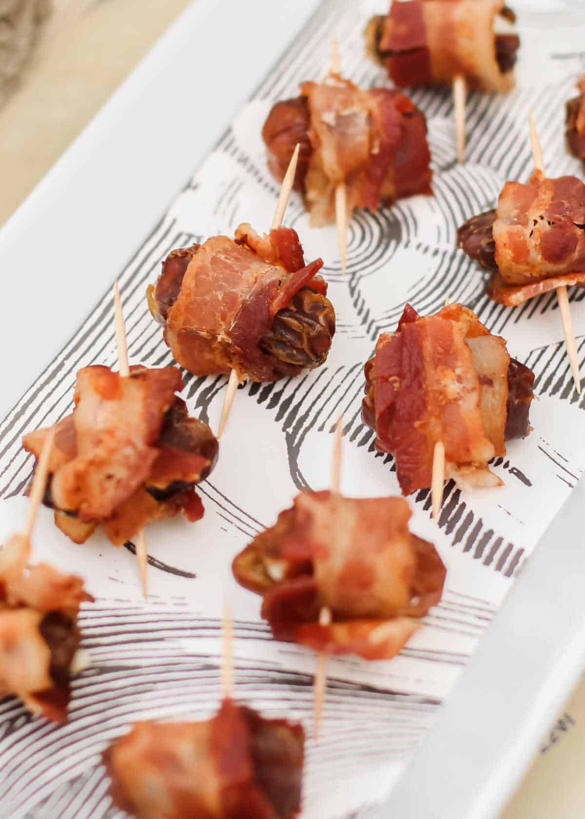 dates wrapped in bacon with toothpicks inserted, on white tray.