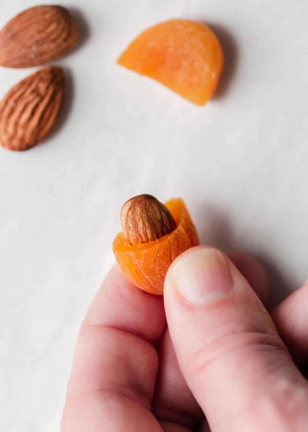 hand holding dried apricot with whole almond inserted into the center.