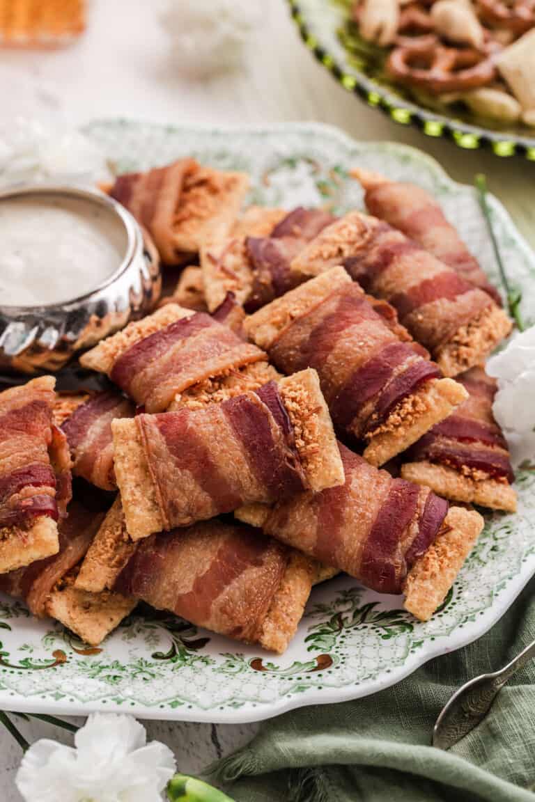 pile of bacon wrapped crackers on green and white vintage plate with small dip bowl.