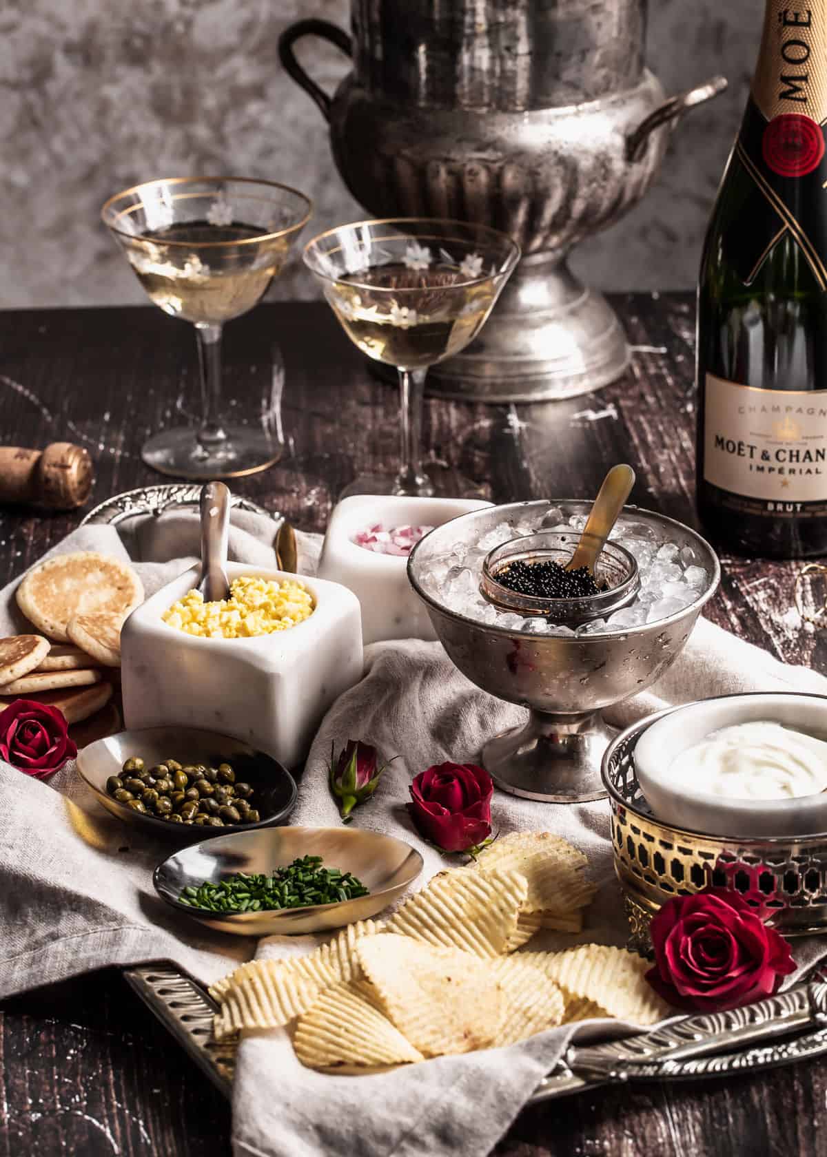 silver tray with caviar and accompaniments, with champagne in background.