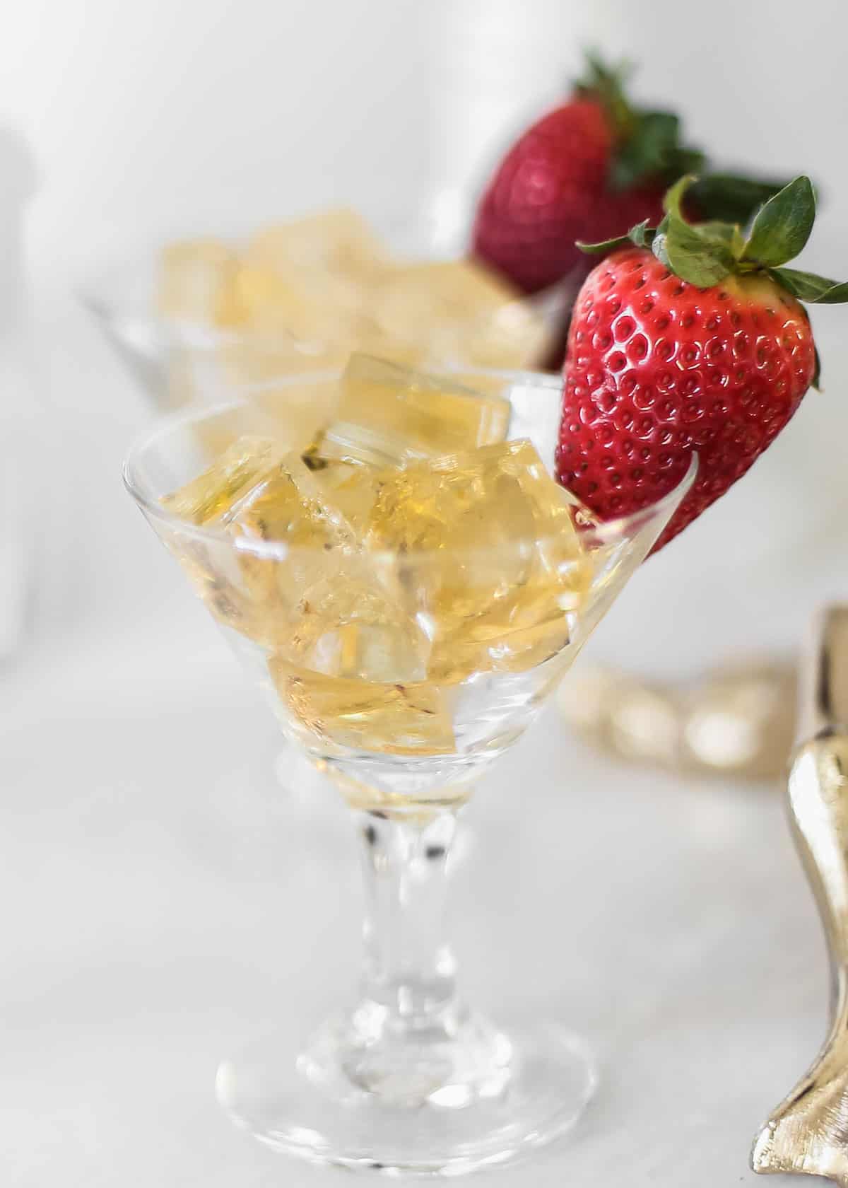 golden colored jello squares in mini martini glasses with strawberry garnish.