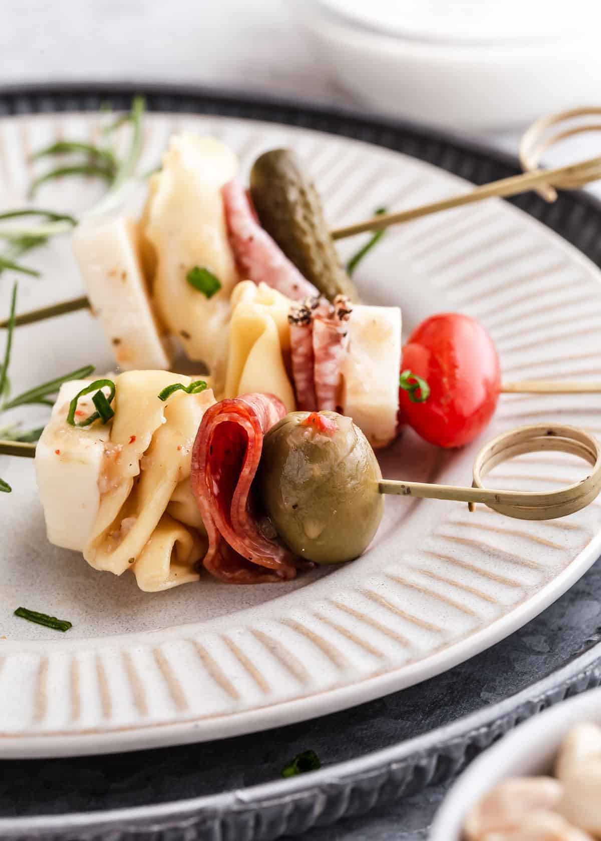 close up of charcuterie skewers on a plate, with tortellini, salami and olives.