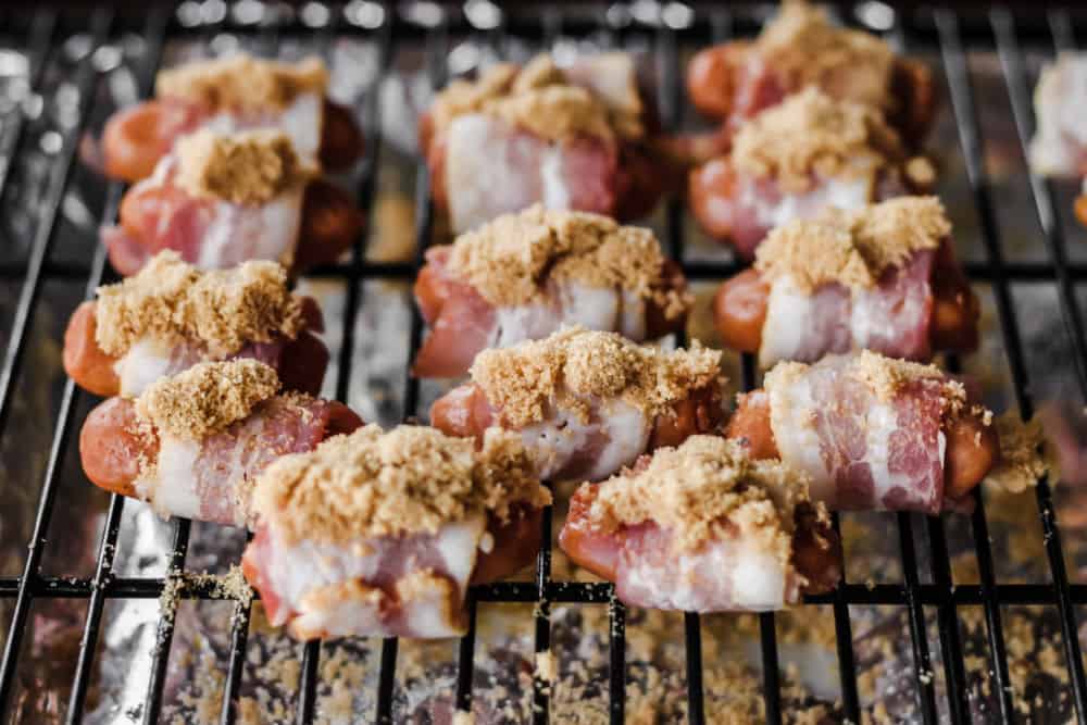bacon wrapped around little smokies and topped with brown sugar, on grill rack in pan in oven.