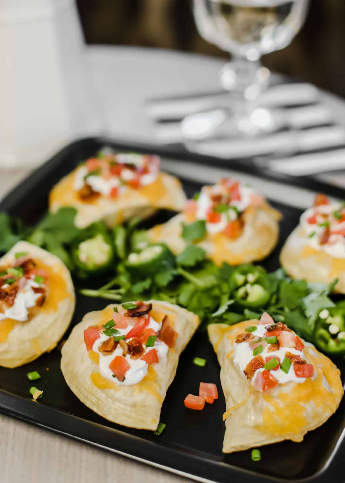 mini pierogis topped with sour cream, tomatoes, bacon and served on black plate.