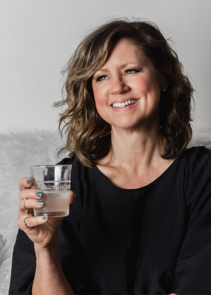 lady in black top holding a drink and smiling.