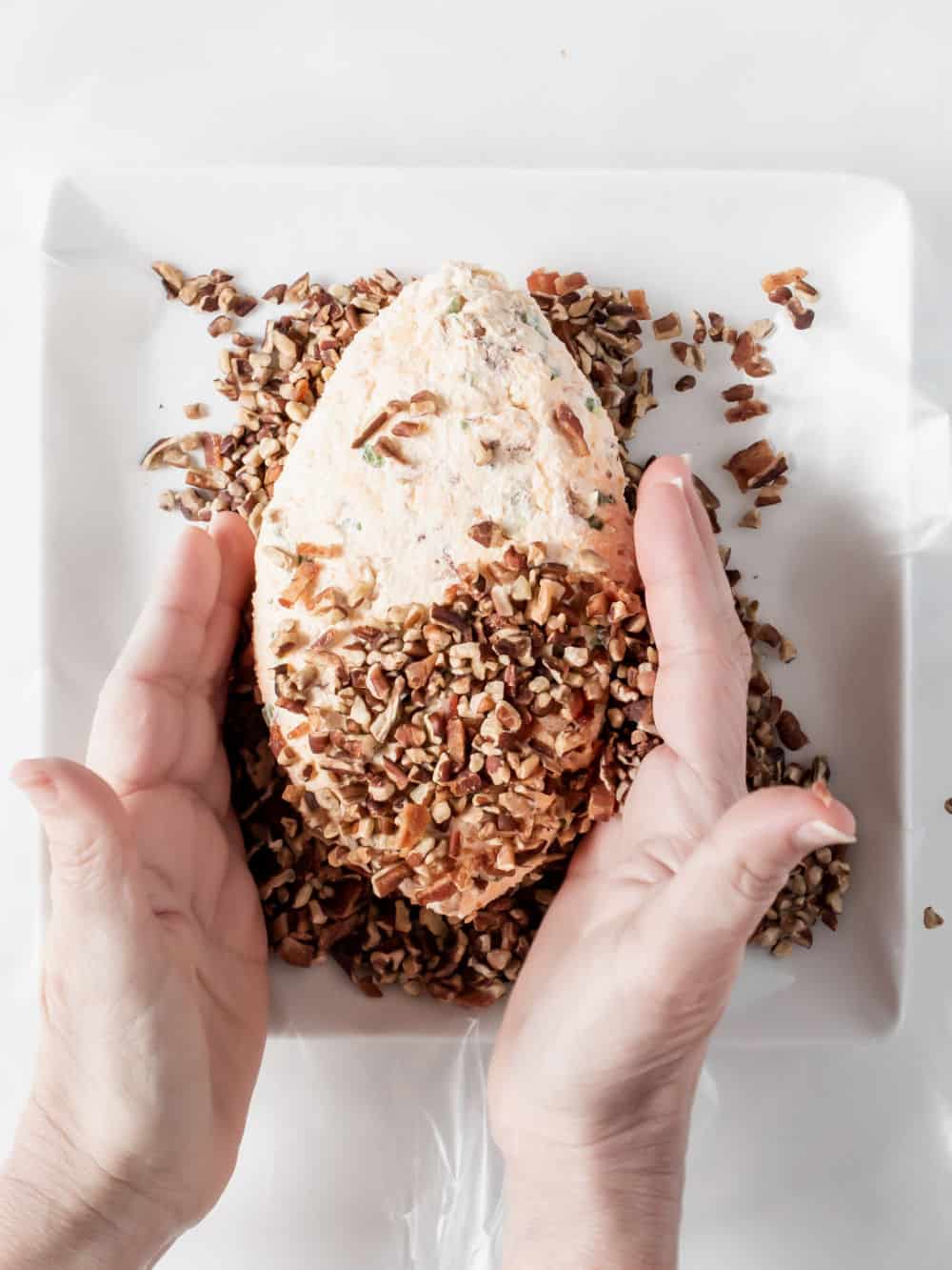 hands adding chopped nuts to football shaped cheese ball,