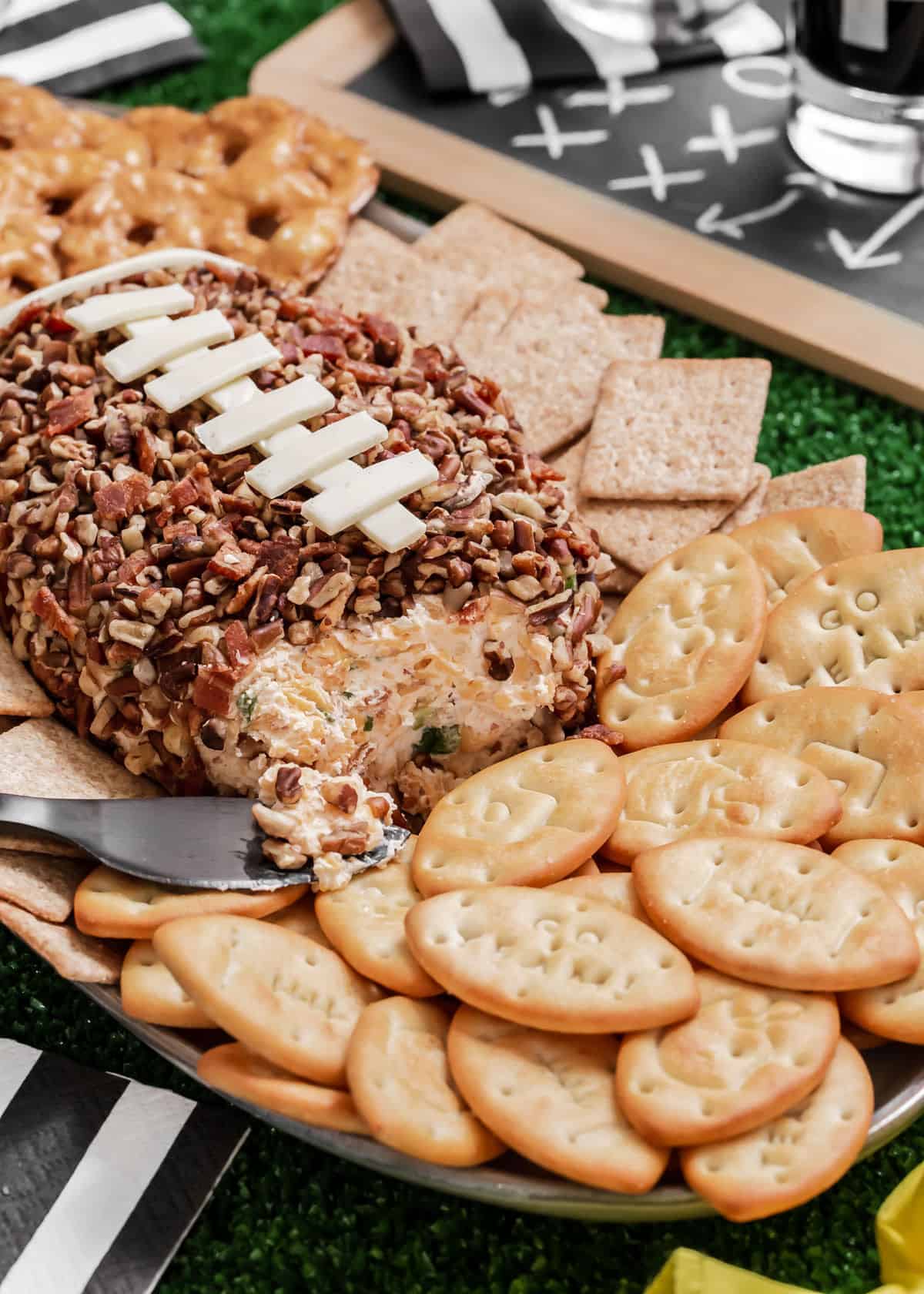 football cheese ball that's been cut into with knife spreader, surrounded by football crackers.