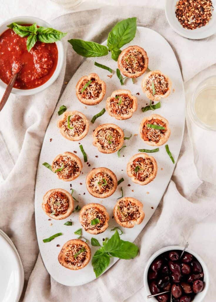 small pastry cups filled with sausage mixture on long platter surrounded by tomato sauce and black olives.