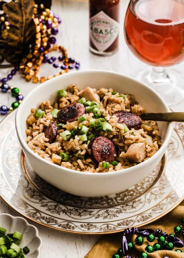 Jambalaya in in bowl sitting on gold edge plate surrounded by Mardi Gras beads.