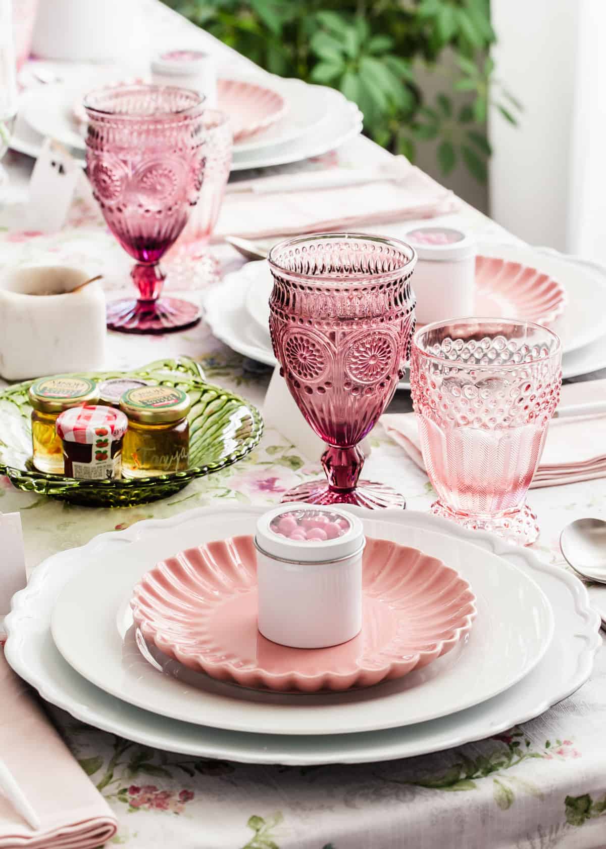 pink and white spring place setting with pink plate on top of white plate and charger and pink glasses and napkins.