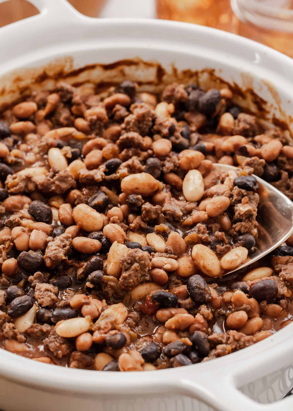 round white baking dish with baked beans and ground beef, with serving spoon.