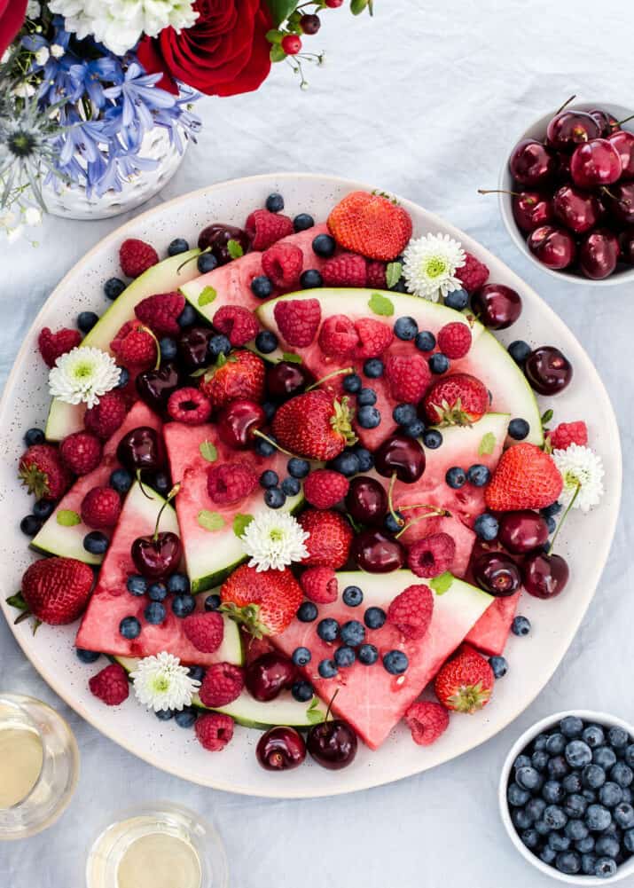 round platter with a mix of fresh berries and watermelon slices, on blue table with overhead view.
