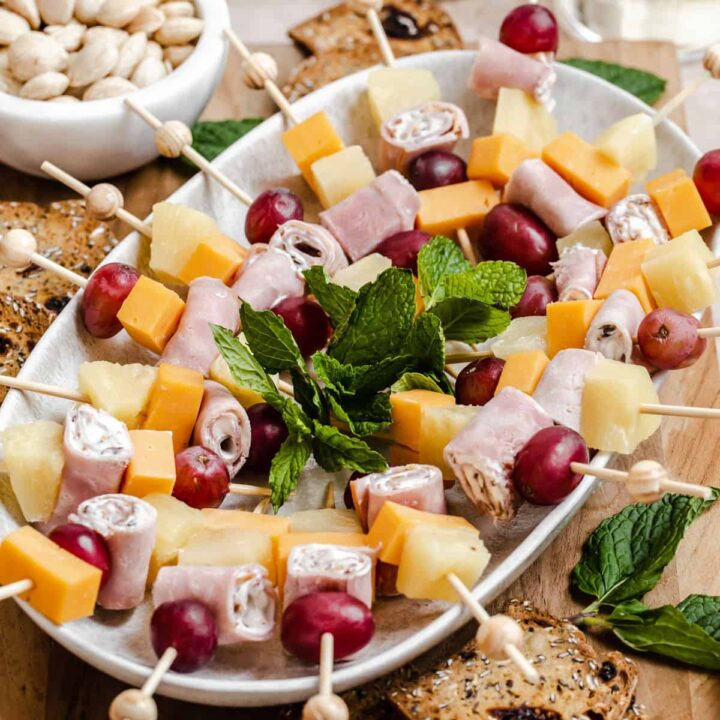 mini fruit and cheese kabobs on oval platter surrounded by crackers, nuts and wine.