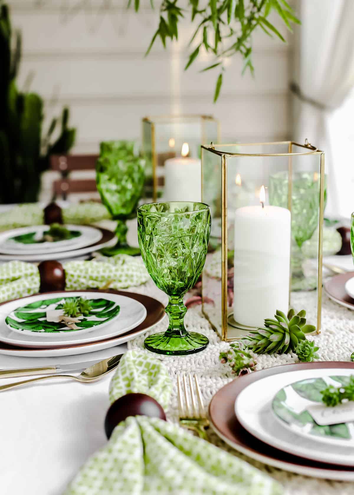 green and cream tablescape outdoors, with green plates and glasses and candle centerpiece.
