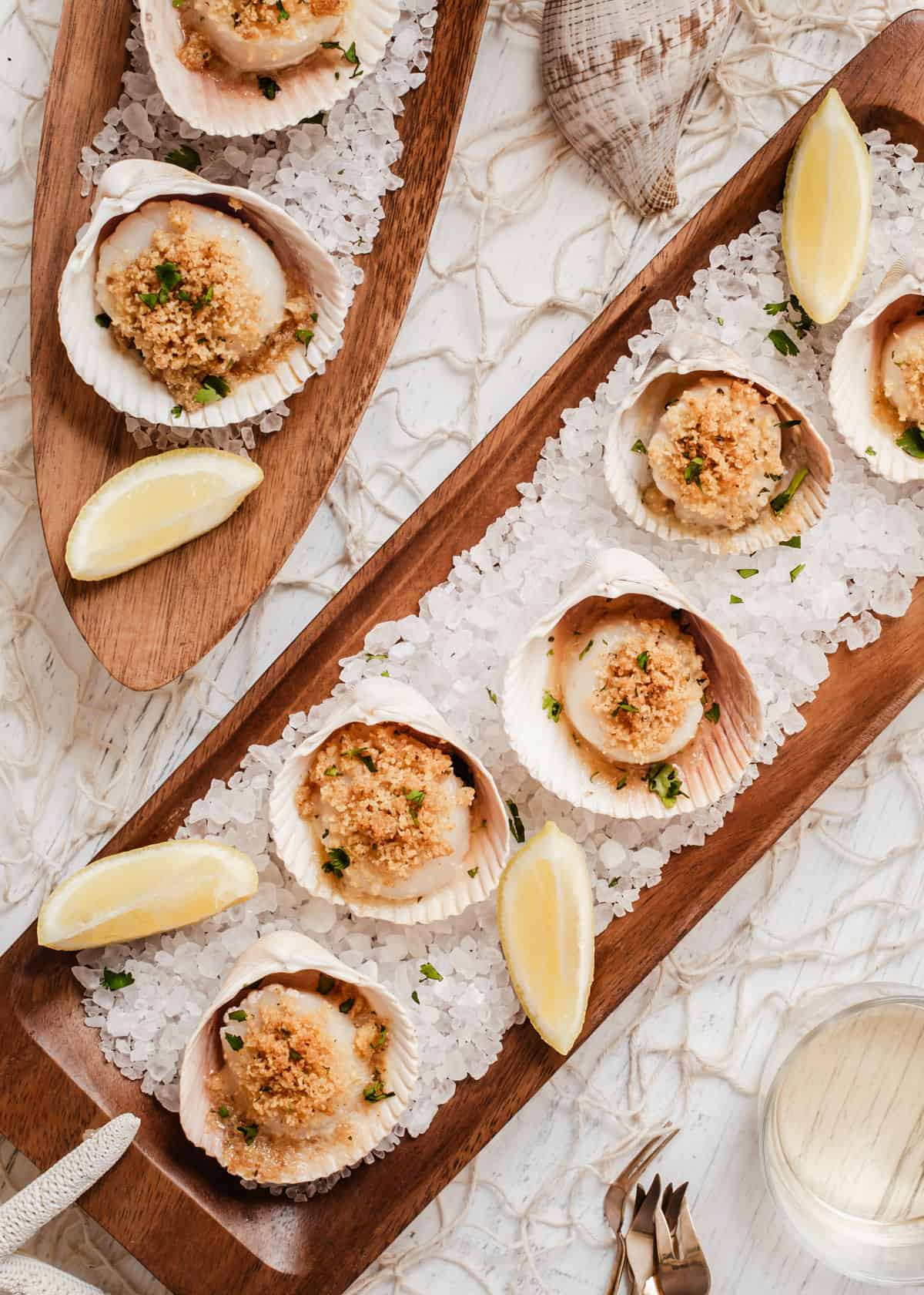overhead view of long wood trays topped with scallops in shells on a bed of rock salt. 