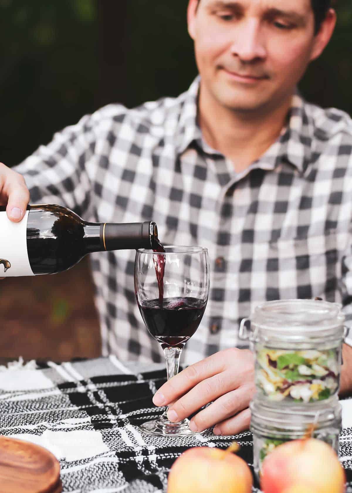 man pouring red wine into glass in outdoor setting.