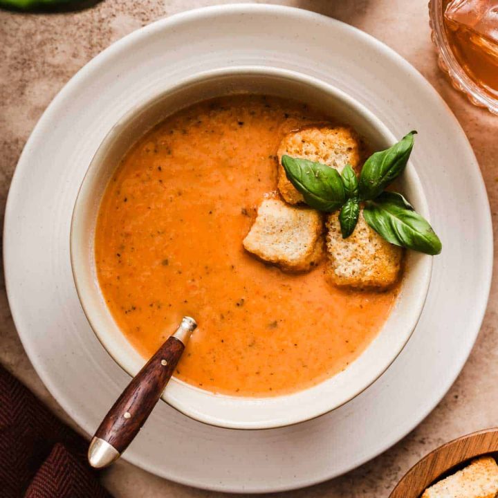 bowl of tomato soup garnished with fresh basil and croutons, on white plate.