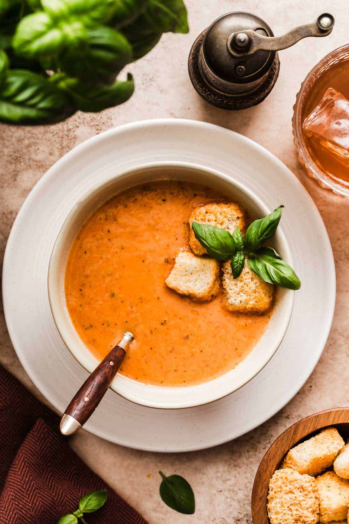 bowl of tomato soup garnished with fresh basil and croutons, on white plate.