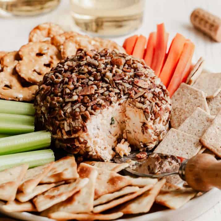 cheese ball on plate with crackers and vegetable sticks.