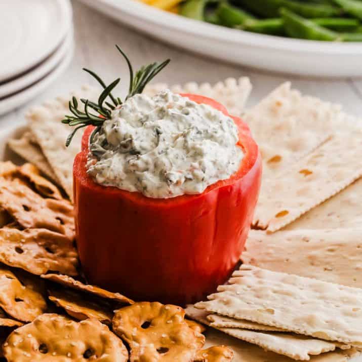 spinach dip served in hollowed out red pepper, with crackers and pretzel crisps.
