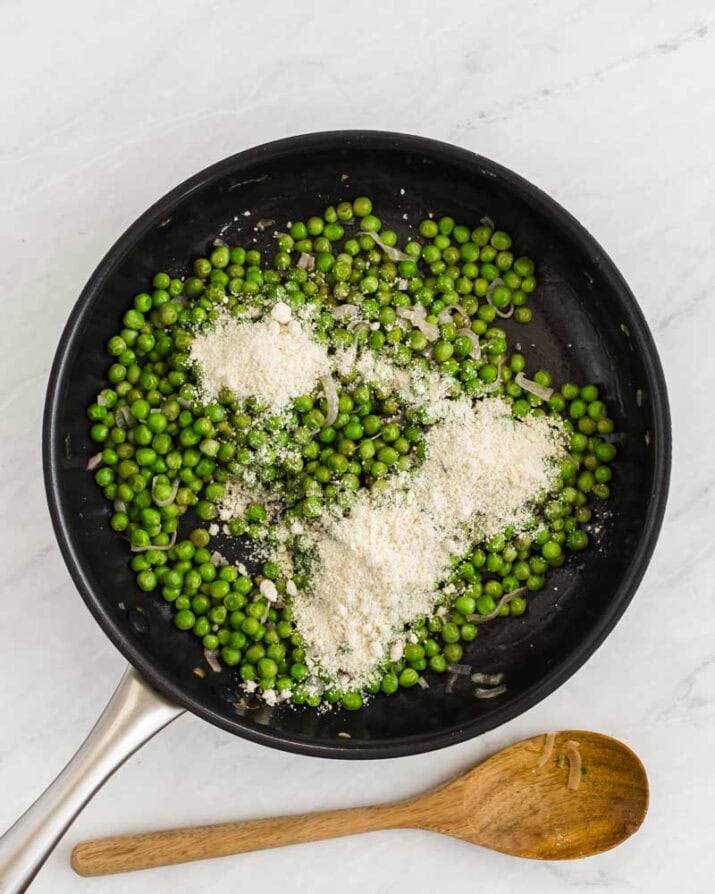 green peas in skillet with grated parmesan on top.