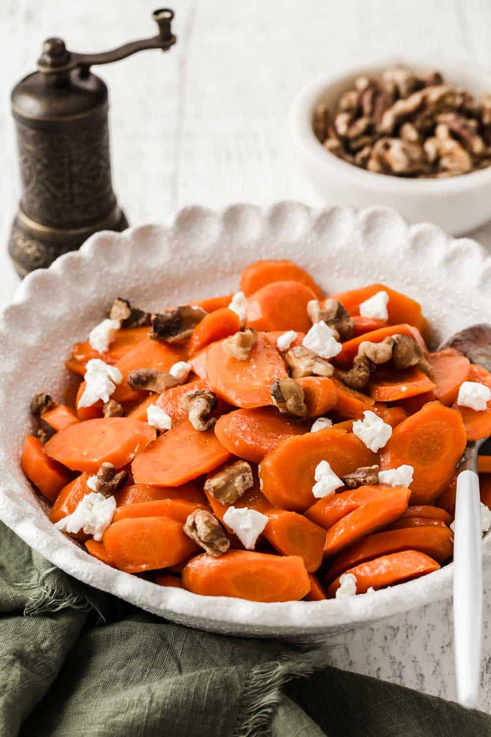 Glazed carrots topped with crumbled goat cheese and walnuts in white serving bowl.