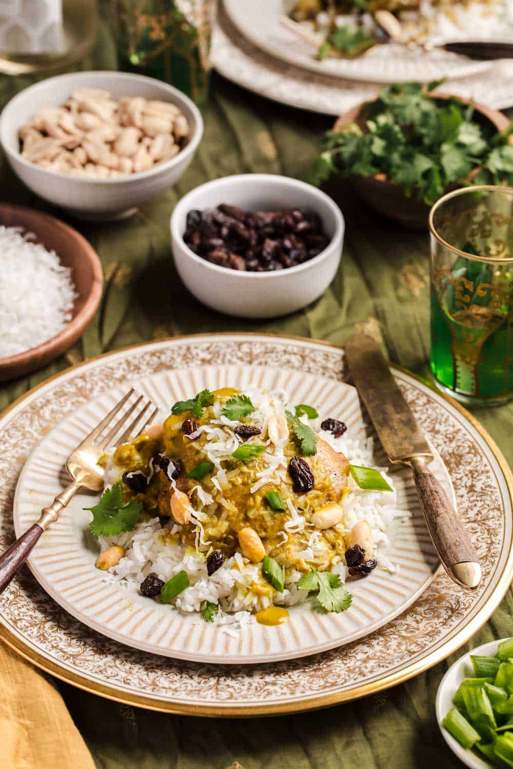 curry chicken meal served on gold trimmed plate with small bowls of toppings around it.