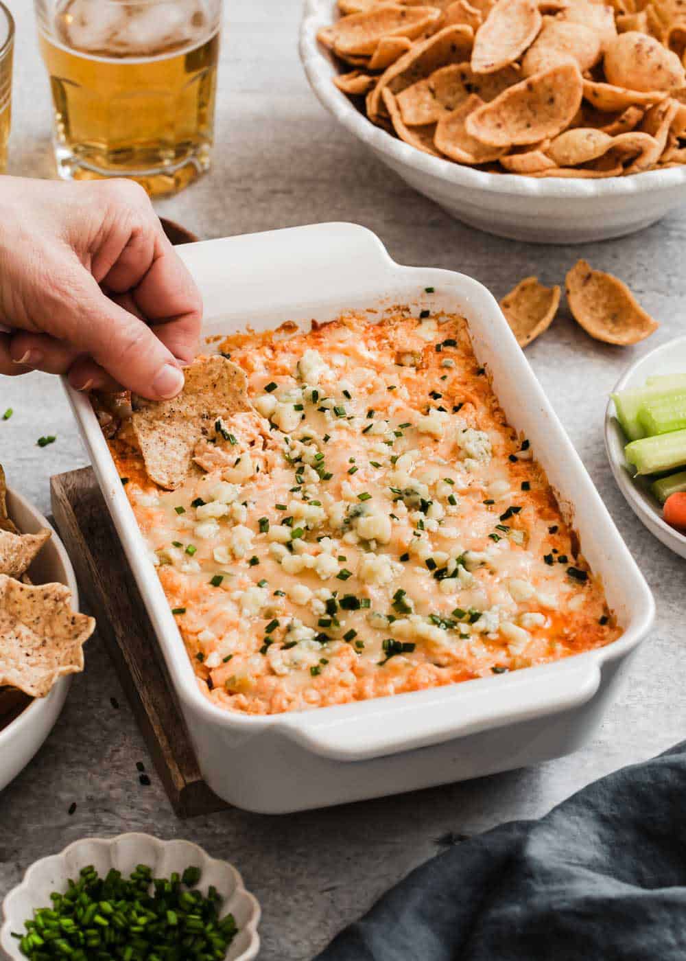 buffalo chicken dip in white baking dish with hand scooping a tortilla chip into it.