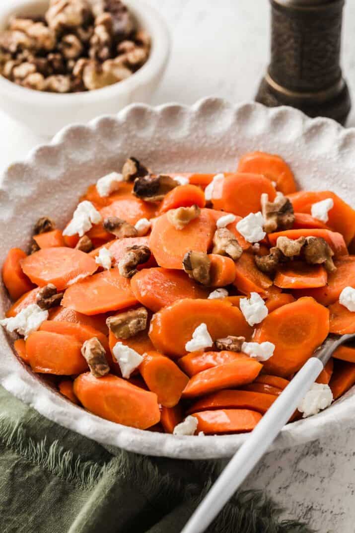 Glazed carrots with walnuts and goat cheese in white serving bowl.