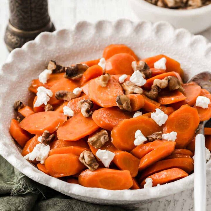 Glazed carrots with walnuts and goat cheese in white serving bowl.