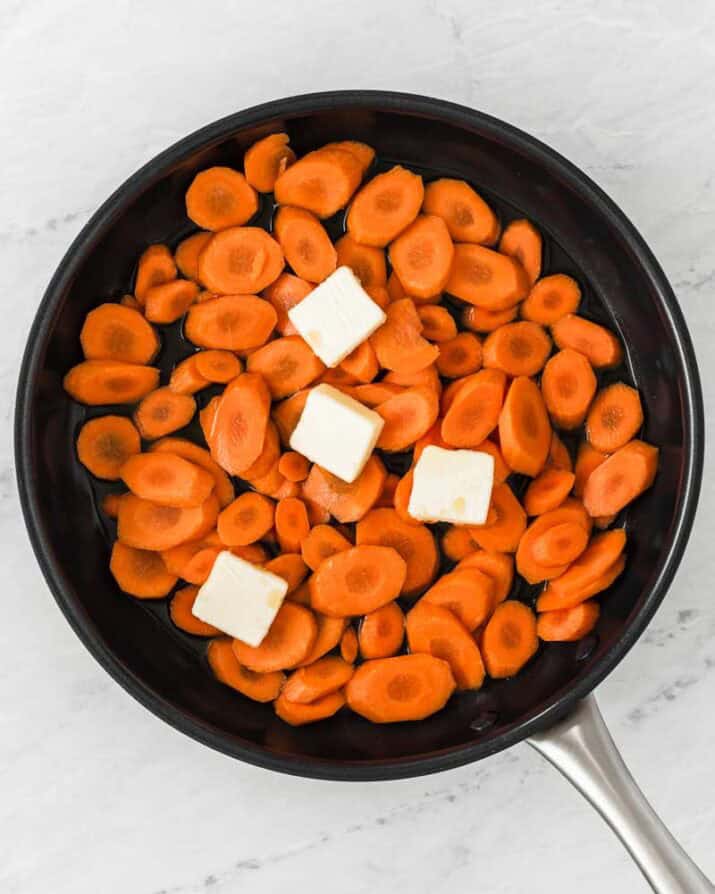 making glazed carrots in a skillet with pats of butter on top.
