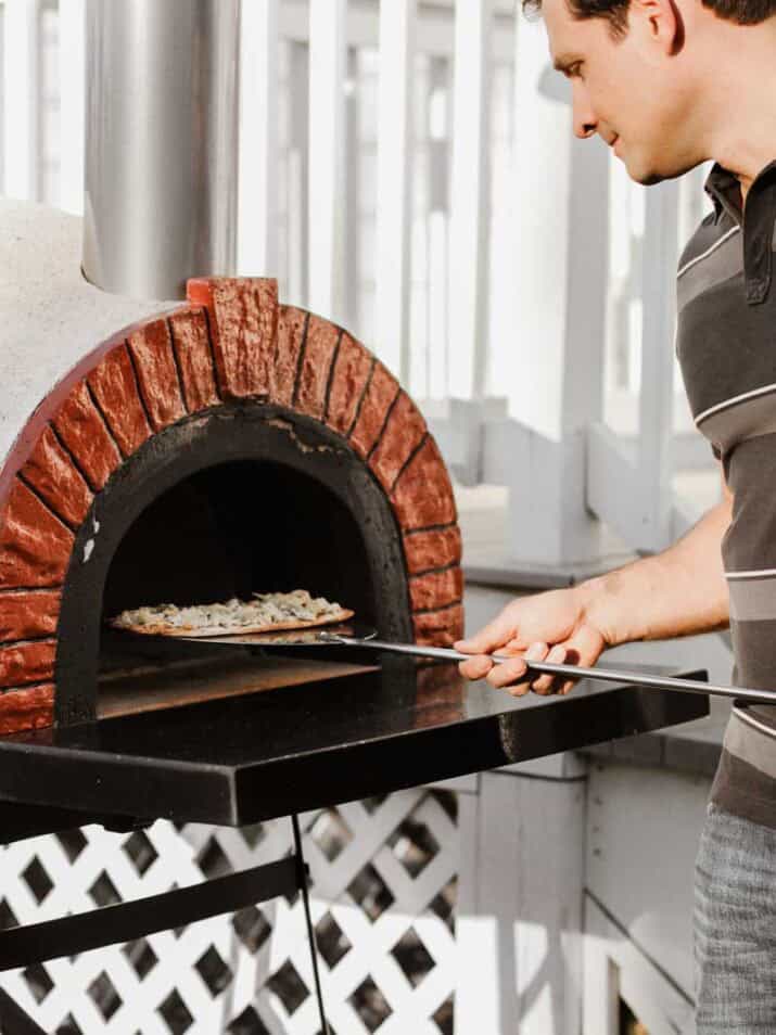 man sliding pizza into pizza oven using a long paddle.