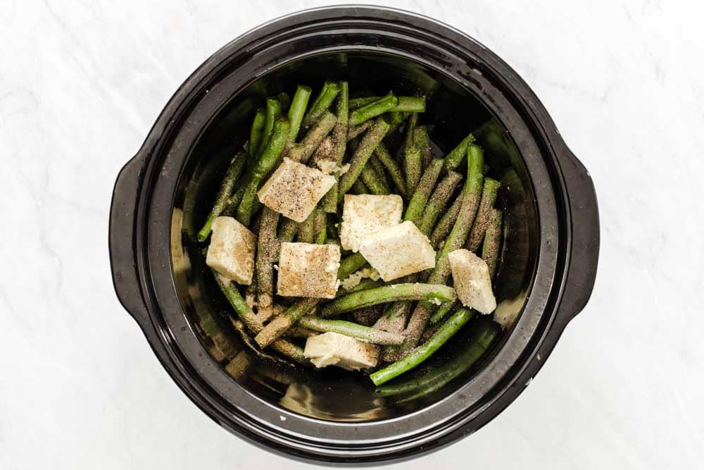 fresh green beans in a crock pot with pats of butter on top.