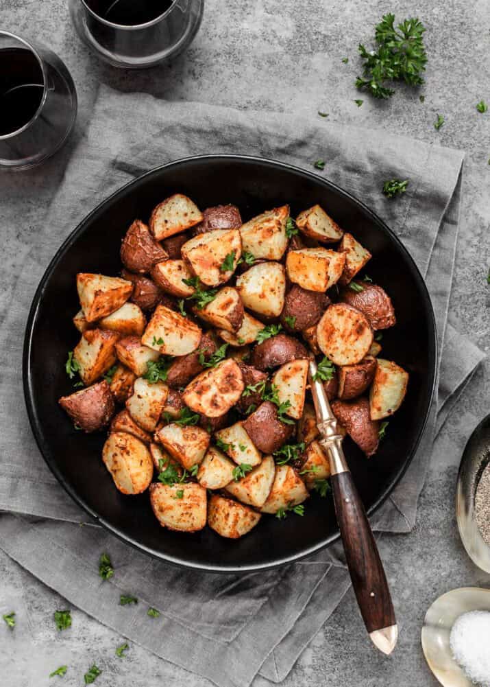 cut roasted potatoes in black serving bowl with spoon.