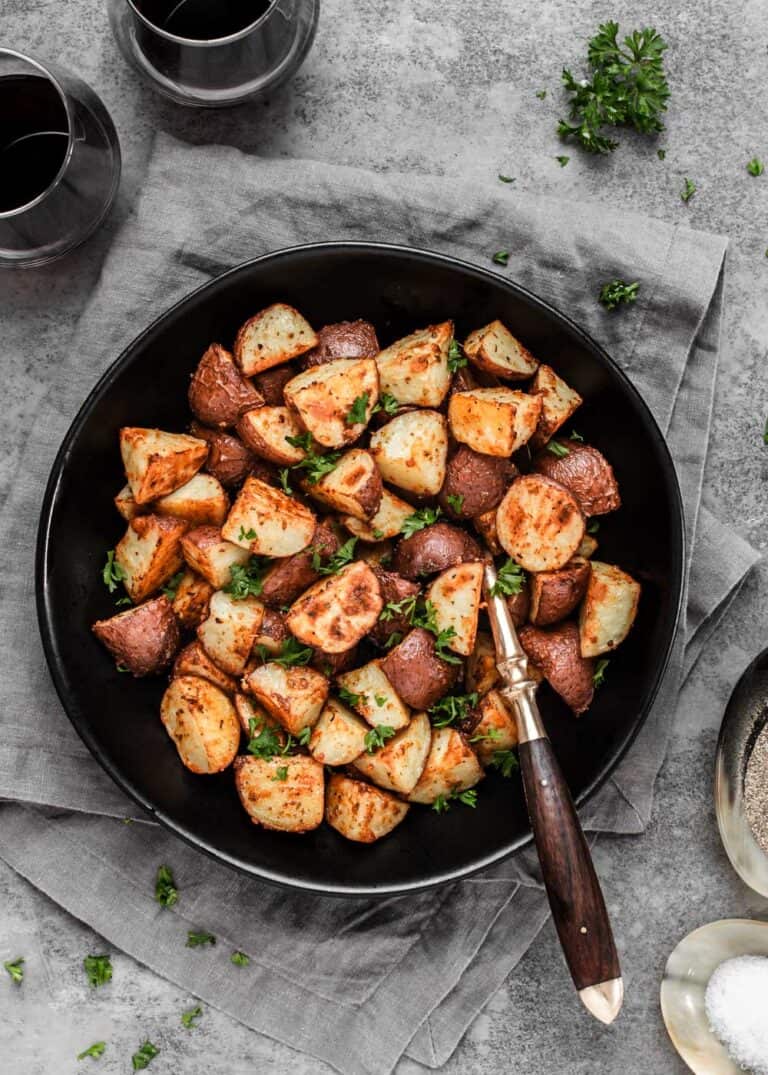 cut roasted potatoes in black serving bowl with spoon.