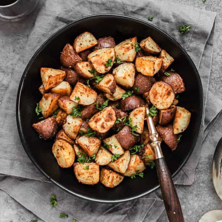 roasted potatoes in black bowl with serving spoon.
