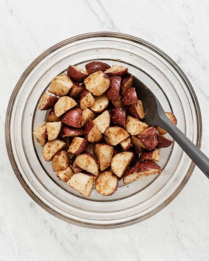 cut potatoes in bowl with seasoning and large spoon.